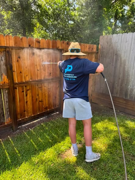 A crew member washing a wood fence in a yard.